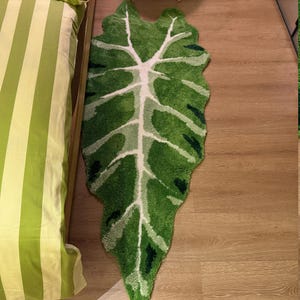 May include: A green and white leaf-shaped rug with a fluffy texture. The rug is laid out on a wooden floor.