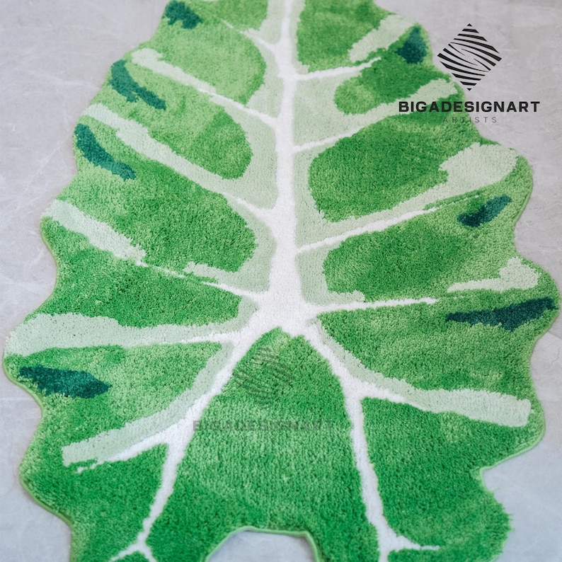 May include: A green and white bath mat shaped like a large leaf. The mat is made of soft, fluffy material and has a white vein pattern.