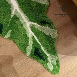 May include: Green, white, and light green leaf-shaped rug with a fuzzy texture. The rug is on a wooden floor.