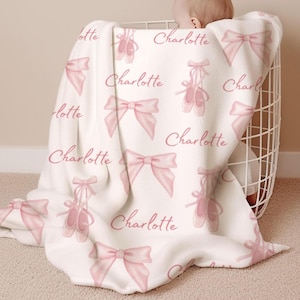 May include: A white fleece baby blanket with a pink ballerina shoe and bow pattern. The blanket is personalized with the name "Charlotte" repeated throughout the design.