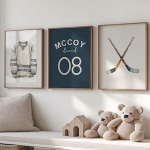 May include: Three framed wall art pieces with a hockey theme. One features a jersey, another a name and number, and the third crossed hockey sticks. The art is in neutral tones with wooden frames, suitable for a nursery or child's room.