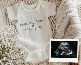 May include: A white baby onesie with the text "coming soon... MAY 2025" on it. The onesie is in a wicker basket with a white blanket and a black and white ultrasound image.