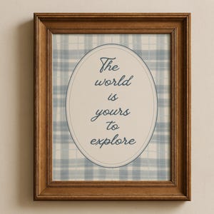 May include: A framed print with a brown wooden frame. The print features a light blue and white plaid background with an oval shape in the center. The oval contains the text "The world is yours to explore" in a cursive font.
