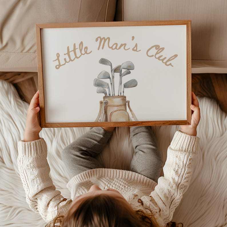 Puede incluir: Una impresi&oacute;n enmarcada con el texto "Little Man's Club" en escritura dorada. La obra de arte presenta una bolsa de golf con palos de golf. El marco es de madera. La impresi&oacute;n es sostenida por una persona.