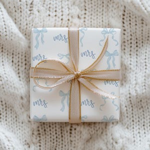 K&ouml;nnte beinhalten: Eine wei&szlig;e Geschenkbox mit goldener Schleife und einem blauen und wei&szlig;en Muster aus Schleifen und dem Wort "mrs." wiederholt.