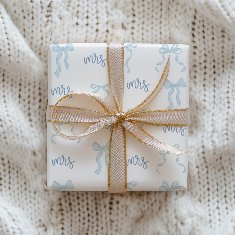 K&ouml;nnte beinhalten: Eine wei&szlig;e Geschenkbox mit goldener Schleife und einem blauen und wei&szlig;en Muster aus Schleifen und dem Wort "mrs." wiederholt.