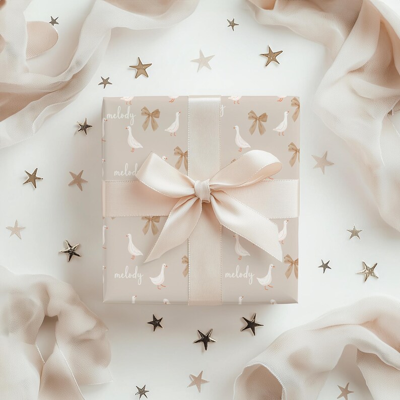 May include: A gift box wrapped in beige paper with a white goose and bow pattern. The box is tied with a light pink satin ribbon and bow. The paper has the word "melody" printed on it. The box is surrounded by gold stars on a white background.