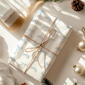 K&ouml;nnte beinhalten: Wei&szlig;e Geschenkpapier mit einem blauen und wei&szlig;en Schleifenmuster und dem Wort "mrs." wiederholt auf der gesamten Fl&auml;che. Das Geschenk ist mit Schnur gebunden.