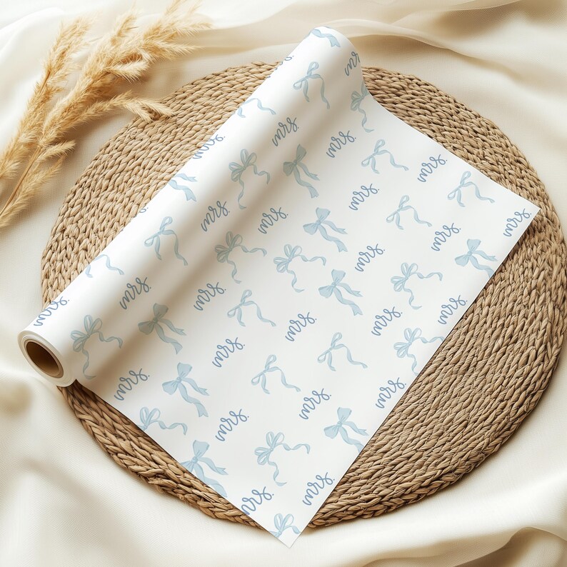 K&ouml;nnte beinhalten: Eine Rolle wei&szlig;es Geschenkpapier mit einem sich wiederholenden Muster aus blauen Schleifen und dem Wort "mrs." in kursivschrift.