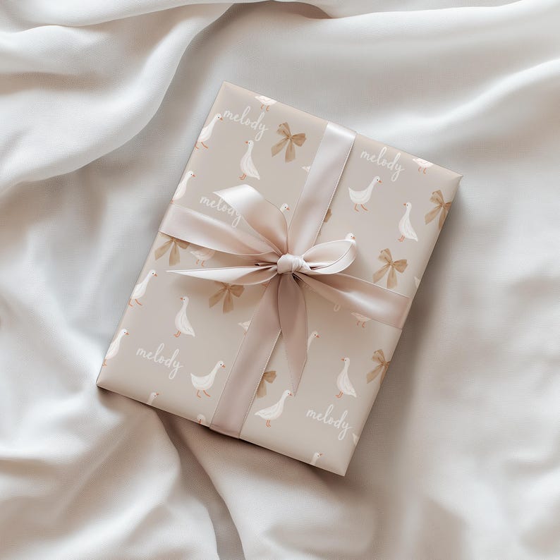 May include: A beige gift box with a white ribbon and a pattern of white geese and bows. The box is wrapped in paper that says "melody" on it.