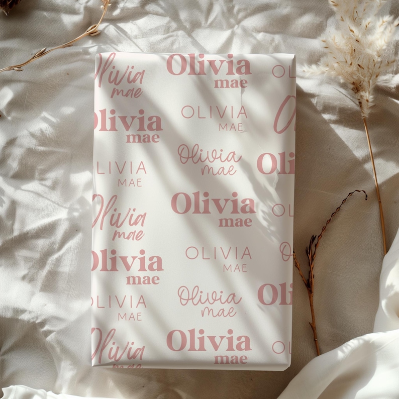 May include: White wrapping paper with a repeating pattern of the name "Olivia mae" in a soft pink color. The names are in a mix of cursive and block letters.