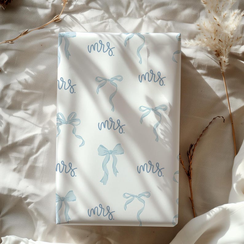 K&ouml;nnte beinhalten: Wei&szlig;e Geschenkpapier mit einem sich wiederholenden Muster aus blauen Schleifen und dem Wort "mrs." in Kursivschrift.
