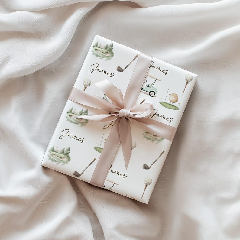 May include: A wrapped gift with golf-themed paper, showing golf clubs, balls, and a cart. It's tied with a light pink satin ribbon. The name "James" is printed on the paper. The gift is on a white satin surface.