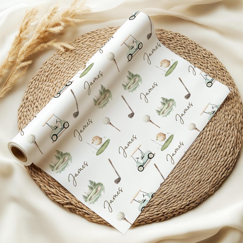 May include: A roll of white wrapping paper featuring a golf-themed design. The pattern includes golf carts, golf balls, golf clubs, and the name "James" in a handwritten style. The illustrations are in green, brown, and beige.