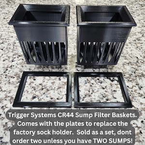 May include: Two black Trigger Systems CR44 sump filter baskets with matching plates. The baskets have a rectangular top and a slotted design on the sides. The text on the image says "Trigger Systems CR44 Sump Filter Baskets."