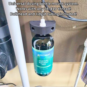 May include: A black dosing bottle mount system with a bottle of Custom Element Mix. The text on the bottle reads "TRITON LAB" and "CUSTOM ELEMENT MIX". The mount system includes bulkhead and rigid tubing. The text above the bottle reads "Universal dosing bottle mount system."