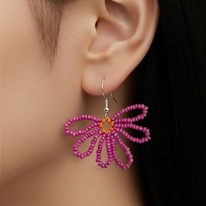 Könnte beinhalten: Ohrring in Form einer Gänseblümchenblüte aus rosa und orangefarbenen Perlen. Die Blütenblätter sind rosa und die Mitte ist orange. Der Ohrring ist an einem silbernen Haken befestigt.
