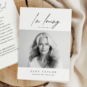 May include: A memorial card featuring a black and white portrait of a woman with long, grey hair. The words "In loving memory" are at the top, with the name "ELEN TAYLOR" and dates below. The card is on a wooden surface.