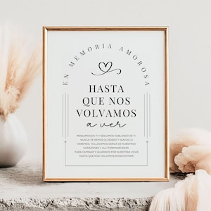 Puede incluir: Un letrero enmarcado con borde dorado y fondo blanco. El letrero presenta texto negro que dice "EN MEMORIA AMOROSA" y "HASTA QUE NOS VOLVAMOS a ver". Un gráfico de corazón está encima del texto.