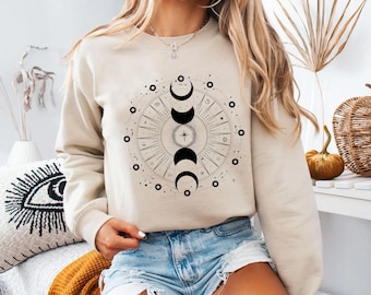 May include: A beige sweatshirt with a black and white moon phase design. The design features a circle with a star in the center and multiple moon phases around the circle.
