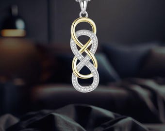 Puede incluir: Collar plateado con un colgante con un símbolo de infinito doble. El colgante tiene un centro dorado y está incrustado con pequeñas piedras preciosas transparentes. El collar cuelga sobre un fondo borroso.