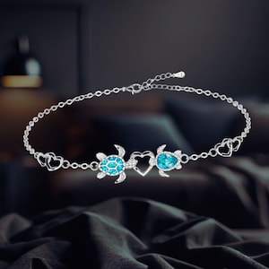 May include: A silver anklet with two turtle charms and a heart charm. The turtles have blue crystal accents.