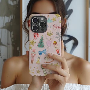 Puede incluir: Una funda de teléfono rosa con un diseño navideño caprichoso. La funda está adornada con ilustraciones de un árbol de Navidad, una bailarina, un cascanueces, estrellas, lazos y otros elementos festivos. Para smartphones.