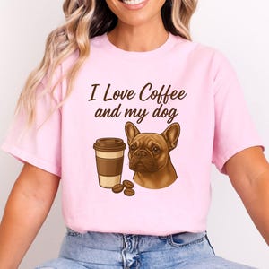 Puede incluir: Camiseta rosa claro con la frase "I Love Coffee and my dog". La camiseta presenta un gráfico de una taza de café, granos de café y un bulldog francés marrón. La camiseta es de material suave.