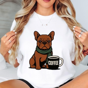 Op de afbeelding: Wit T-shirt met een bruine Franse bulldog met een groene sjaal, naast een zwarte koffiemok met "COFFEE" in het wit. Een eenvoudige, schattige illustratie.