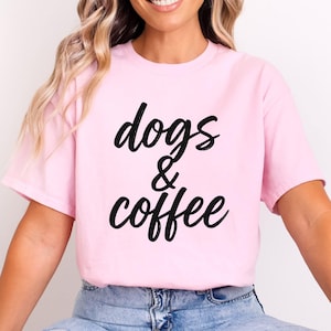 Könnte beinhalten: Hellrosa T-Shirt mit dem schwarzen Schriftzug "dogs & coffee". Das Shirt besteht aus einem weichen Material und hat kurze Ärmel. Das Model trägt eine blaue Jeans.