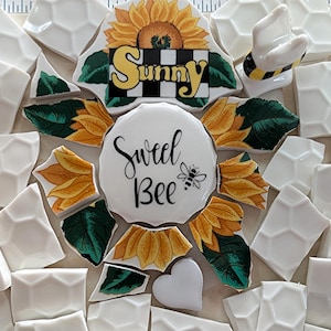 May include: A mosaic design featuring a sunflower with the word "Sunny" on a checkered background. The mosaic includes a white circle with "Sweet Bee" and a bee graphic, surrounded by sunflower petals and white geometric tiles.
