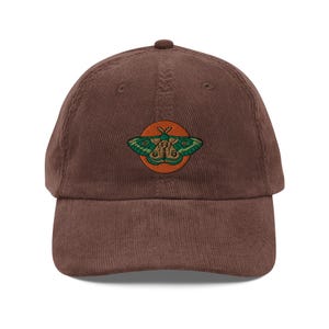 May include: A brown corduroy baseball cap with an embroidered green and orange moth design.
