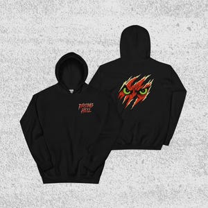 May include: Black hooded sweatshirt with the text "Raising Hell" in red on the front. The back of the sweatshirt features a graphic of red claw marks revealing a red and yellow face with green eyes. The sweatshirt has a front pocket and a hood.