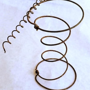 May include: A rusty brown metal coil spring with a spiral top and a series of circular coils. The spring has a vintage appearance, suggesting it may be an antique or reclaimed item. The design is simple and functional.