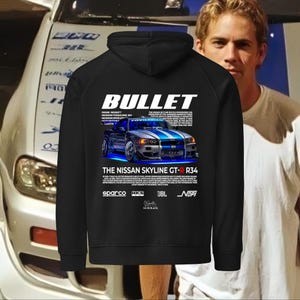 Könnte beinhalten: Schwarzer Kapuzenpullover mit einer Grafik eines blau-silbernen Nissan Skyline GT-R R34, darüber das Wort "BULLET". Der Hoodie hat auch den Text "THE NISSAN SKYLINE GT-R R34" und verschiedene Markenlogos.