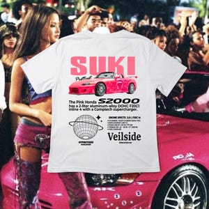 Peut inclure: T-shirt blanc avec un motif rose d'une Honda S2000, le texte "SUKI Prettiest", et le texte "The Pink Honda S2000 has a 2-liter aluminium-alloy DOHC F20C1 inline 4 with a Comptech supercharger." Le motif comprend également un globe avec le texte "Hypnotized Worldwide" et le texte "Veilside Streetglow".