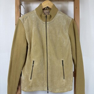 May include: A tan suede jacket featuring long ribbed knit sleeves and a matching ribbed mock neck collar. The jacket includes a full-length central zipper closure and two vertical zippered pockets on the front, providing a structured look.
