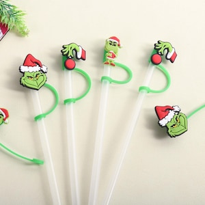 Puede incluir: Pajitas de plástico transparente con adornos verdes con temática de Grinch. Los adornos presentan al Grinch con un gorro de Papá Noel, una mano verde y un adorno rojo. Las pajitas están diseñadas para uso festivo navideño.