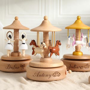 Peut inclure: Trois boîtes à musique carrousel en bois. L'une présente deux danseuses, une autre des chevaux et la dernière des licornes. Chacune porte un nom différent gravé sur la base. Les toits des carrousels sont brun clair et jaunes.
