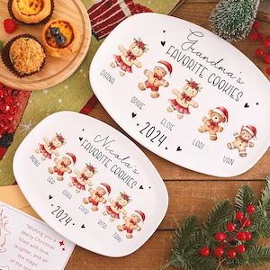 May include: Two white oval platters with gingerbread people illustrations and the text "Grandma's Favorite Cookies" and "Nicola's Favorite Cookies" with names and the year 2024. The platters are on a wooden surface.