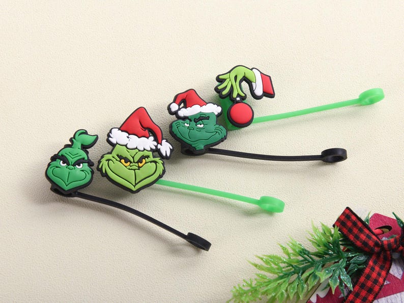 May include: Green Grinch-themed silicone cable ties. Each tie features a different Grinch design, including his face and hand holding an ornament. The ties have black and green stems and are perfect for organizing cables.