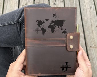 May include: A brown leather journal with a world map design and an airplane graphic. The journal has a pen holder and a snap closure. The initials "J" and "ROBERT" are engraved on the cover.