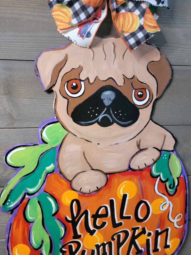 May include: A wooden pug dog decoration sitting on a pumpkin with the words "hello Pumpkin". The pumpkin is orange with green leaves and purple accents. A bow with pumpkins and a black and white checkered pattern is at the top.