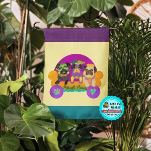 May include: A Mardi Gras themed garden flag with three pugs wearing festive costumes and riding in a float. The flag is yellow, purple, and green with the text "Mardi Paws".