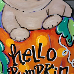May include: A hand-painted wooden sign featuring a pug dog sitting on an orange pumpkin. The sign has the words "hello Pumpkin" in black and white lettering. The pumpkin has yellow polka dots and green leaves.