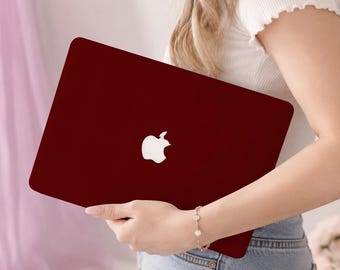 May include: A deep burgundy laptop case featuring a smooth, matte finish and a central white Apple logo cutout. The protective cover is designed to fit securely over the exterior of the laptop, providing a solid, uniform colour across the surface.