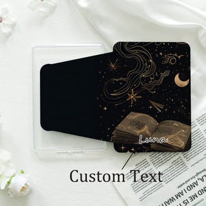 May include: Black phone case with a celestial design featuring gold stars, a crescent moon, and an open book with the name "Luna". The case is next to a clear phone case and a newspaper with the text "Custom Text".