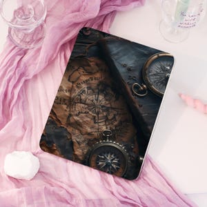 May include: A tablet case featuring a vintage map design with compasses. The case has a dark leather-like texture and a detailed nautical chart print. The compasses are metallic with intricate detailing, evoking a sense of exploration and adventure.