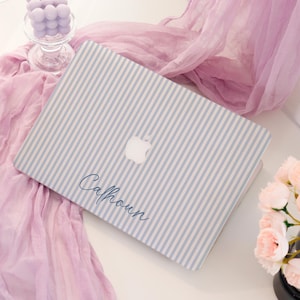 May include: A laptop with a light blue and white striped pattern. The Apple logo is visible on the cover. The name "Calhoun" is written in cursive on the cover.