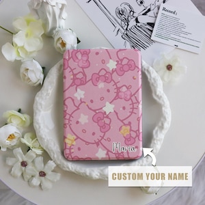 May include: Pink rectangular case featuring a repeating pattern of Hello Kitty faces, bows, and stars. The case has the name "Maria" in cursive and the text "CUSTOM YOUR NAME" below. The case is surrounded by white flowers.